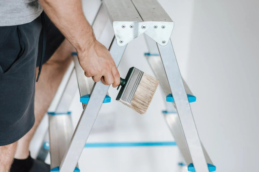 Painter with paint brush climbing a step ladder